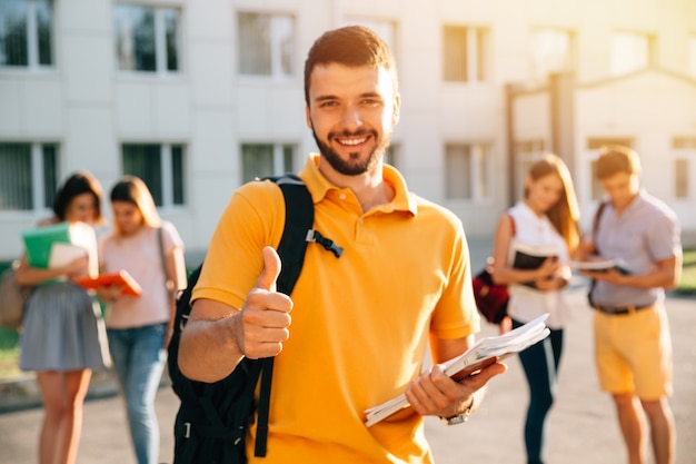 Young attractive smiling student showing thumb up outdoors on campus at the university. Free Photo